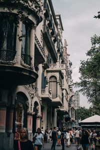 People on street amidst buildings in city against sky