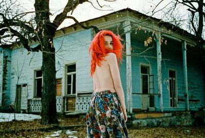 Portrait of shirtless woman standing against house