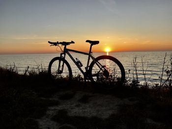 Bicycle by sea against sunset sky