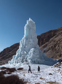 People on snowcapped mountain against clear sky