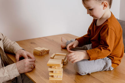 Father and son sitting together at home and playing with wooden blocks. jenga game. 