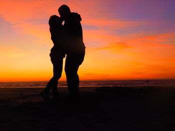 Silhouette man standing on beach against orange sky