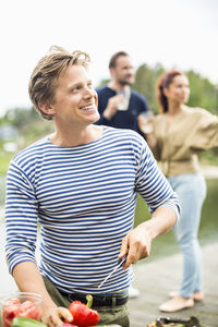 Man looking away while chopping bell pepper with friends standing in background