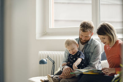 Little boy sittiing on father's lap, mother reading out children's book