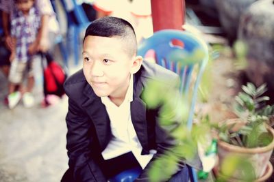 Boy in suit looking away while sitting on chair