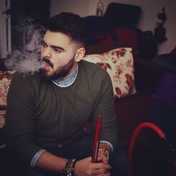 Young man smoking hookah while sitting at home