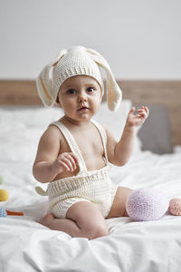 Portrait of cute baby girl sitting on bed at home