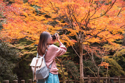 Woman with autumn leaves standing by tree