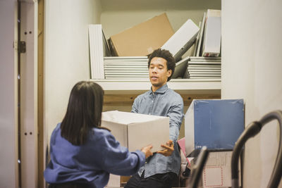 Salesman giving appliance to saleswoman while standing in electronics store