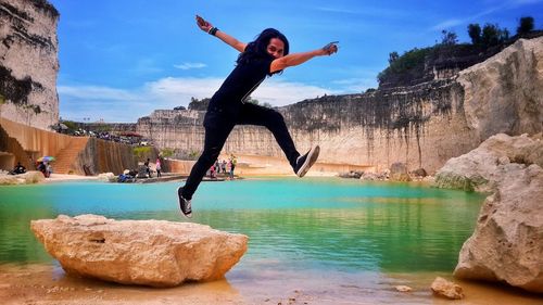 Man jumping on rock at shore against sky