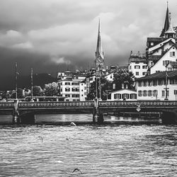 View of river by buildings against cloudy sky