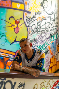 Portrait of young man standing against graffiti wall