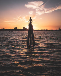 Silhouette structure in sea against sky during sunset