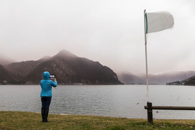 Rear view of woman photographing lake against sky