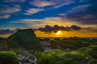 Rocks by sea against sky during sunset