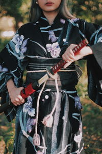 Midsection of woman with umbrella standing on field