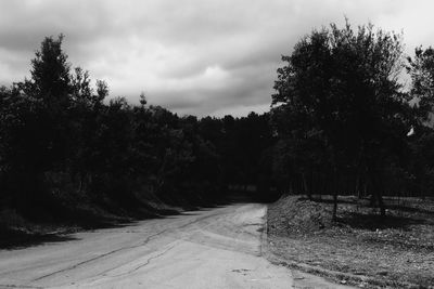 Dirt road passing through landscape against cloudy sky