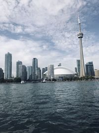 Sea and buildings in city against cloudy sky