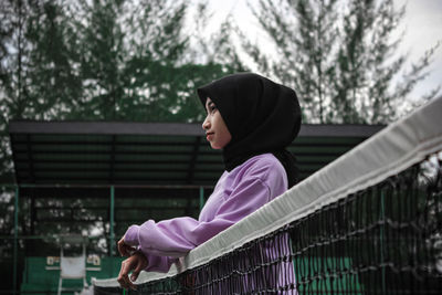 Side view of woman looking away while sitting on railing