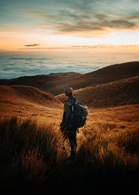 Rear view of woman walking on field against sky during sunset