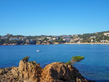 Scenic view of sea by townscape against clear blue sky