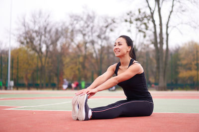 Smiling woman stretching while sitting at court