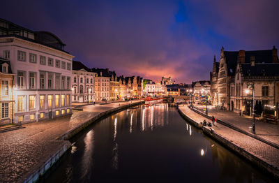 Canal amidst illuminated buildings in city at night