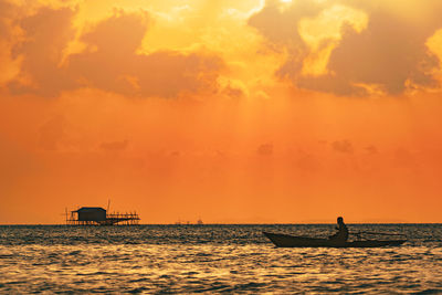 Silhouette man on boat in sea against sky during sunset