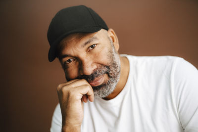 Mature man wearing cap with hand on chin in studio