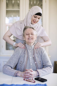 Young female home caregiver giving shoulder massage to grandmother at home