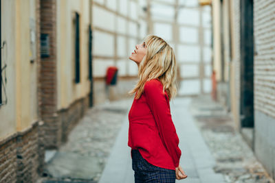 Side view of a young woman standing against building