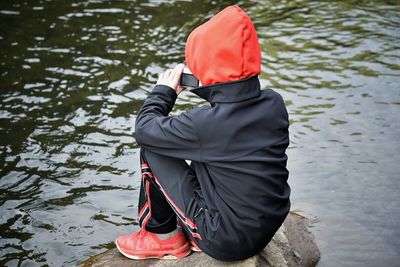 Boy photographing of river through camera while sitting on rock