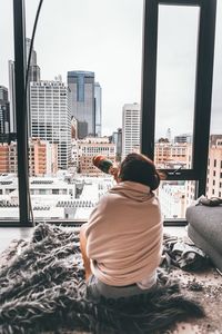 Rear view of man sitting against buildings in city