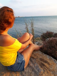 Woman sitting on rock looking at view of sea against sky