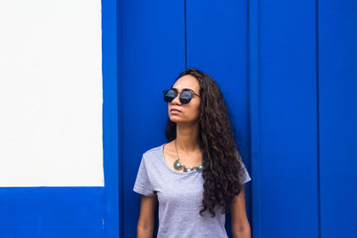 Woman wearing sunglasses standing against blue wall outdoors