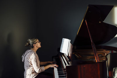 Side view of mature woman playing piano at home