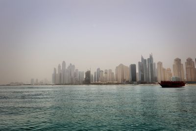 Sea by buildings in city against clear sky