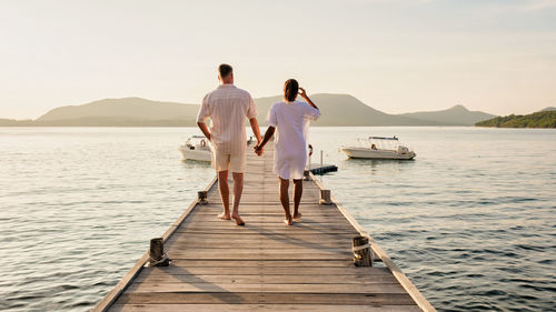 Rear view of woman walking on pier over sea against sky