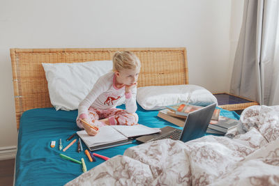 Girl with books using laptop on bed at home