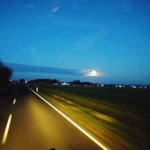 Illuminated road against clear blue sky at night