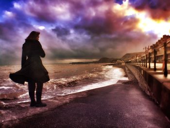 Silhouette of people standing by sea against cloudy sky