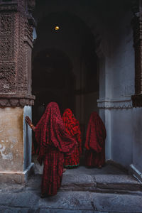 Rear view of women standing in red traditional clothing at temple