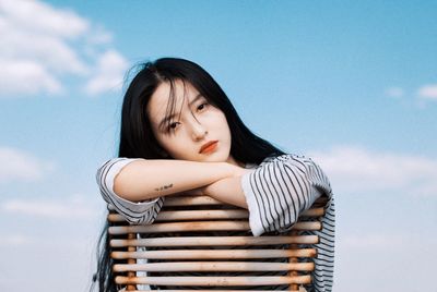 Portrait of young woman sitting on chair against sky