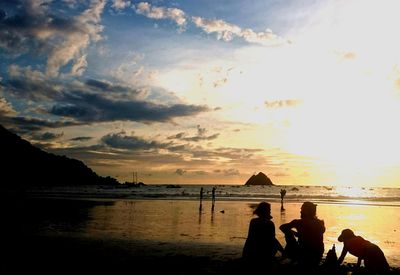 Silhouette people on beach against sky during sunset