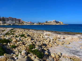 Scenic view of sea by buildings against clear blue sky