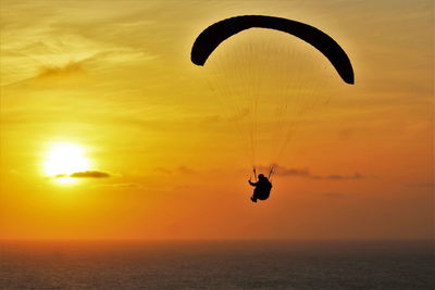 Silhouette of person paragliding at sunset