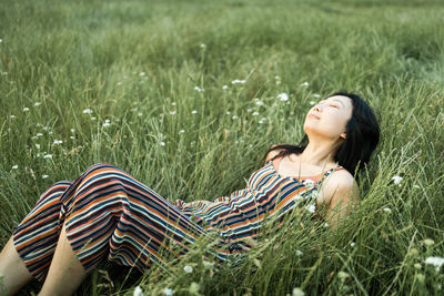 Asian girl lying in green field with wild flowers.