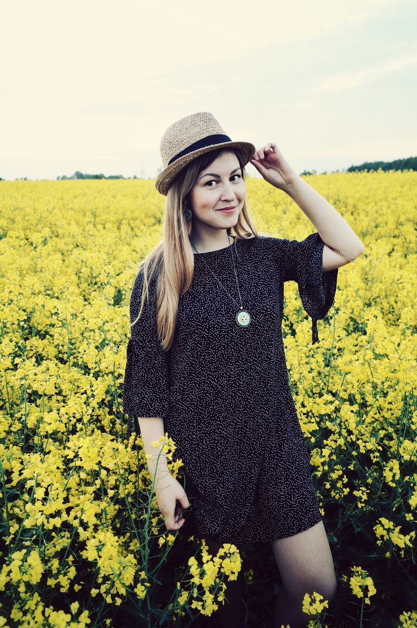 one person, young women, yellow, young adult, plant, real people, field, standing, leisure activity, beauty in nature, hat, land, beautiful woman, beauty, flowering plant, three quarter length, casual clothing, nature, flower, hair, hairstyle, outdoors, teenager