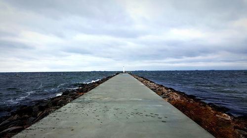 Surface level of pier over calm sea against cloudy sky