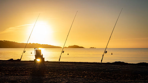 Silhouette fishing net on beach against sky during sunset